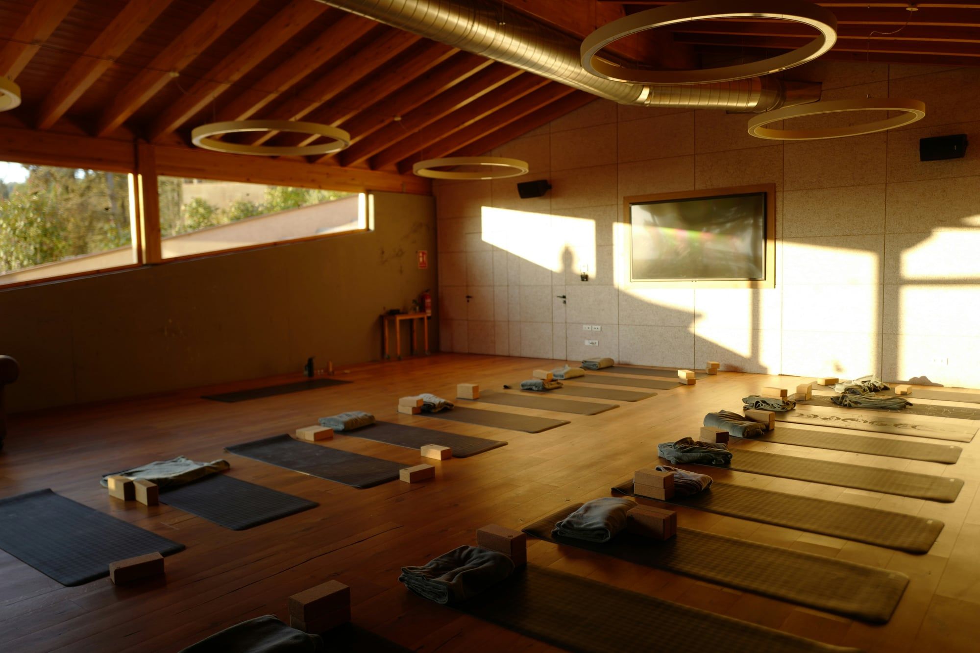 An empty yoga studio with mats and blocks laid out on a wooden floor in the evening sun