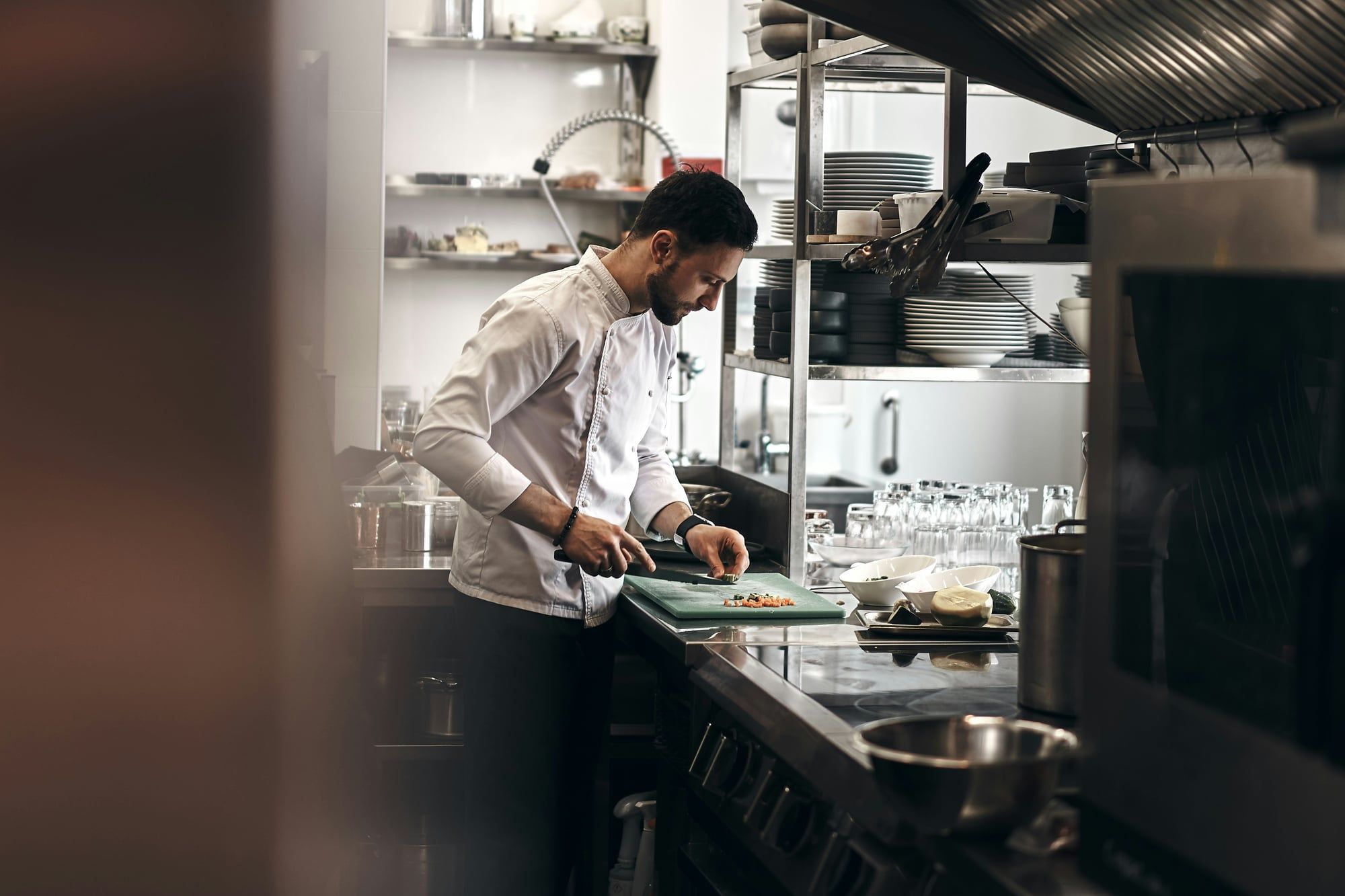 A chef in a white jacket chops vegetables in a restaurant kitchen
